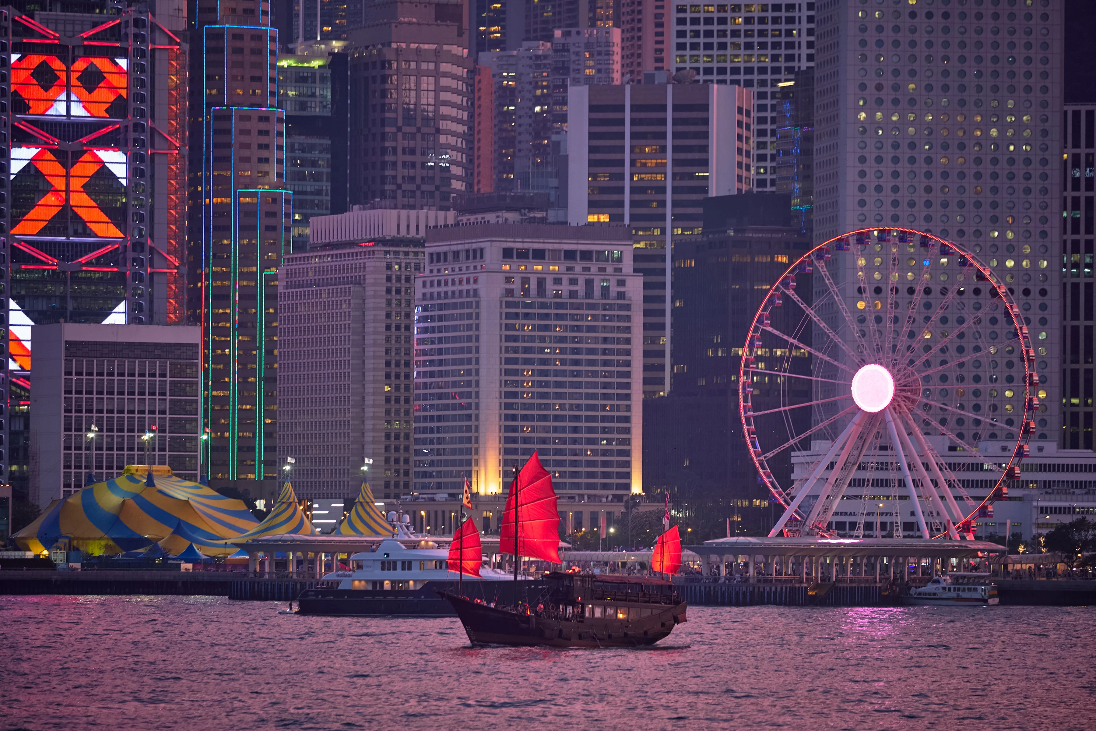 Jonque rouge aux voiles &eacute;carlates devant le skyline illumin&eacute; de Hong Kong la nuit