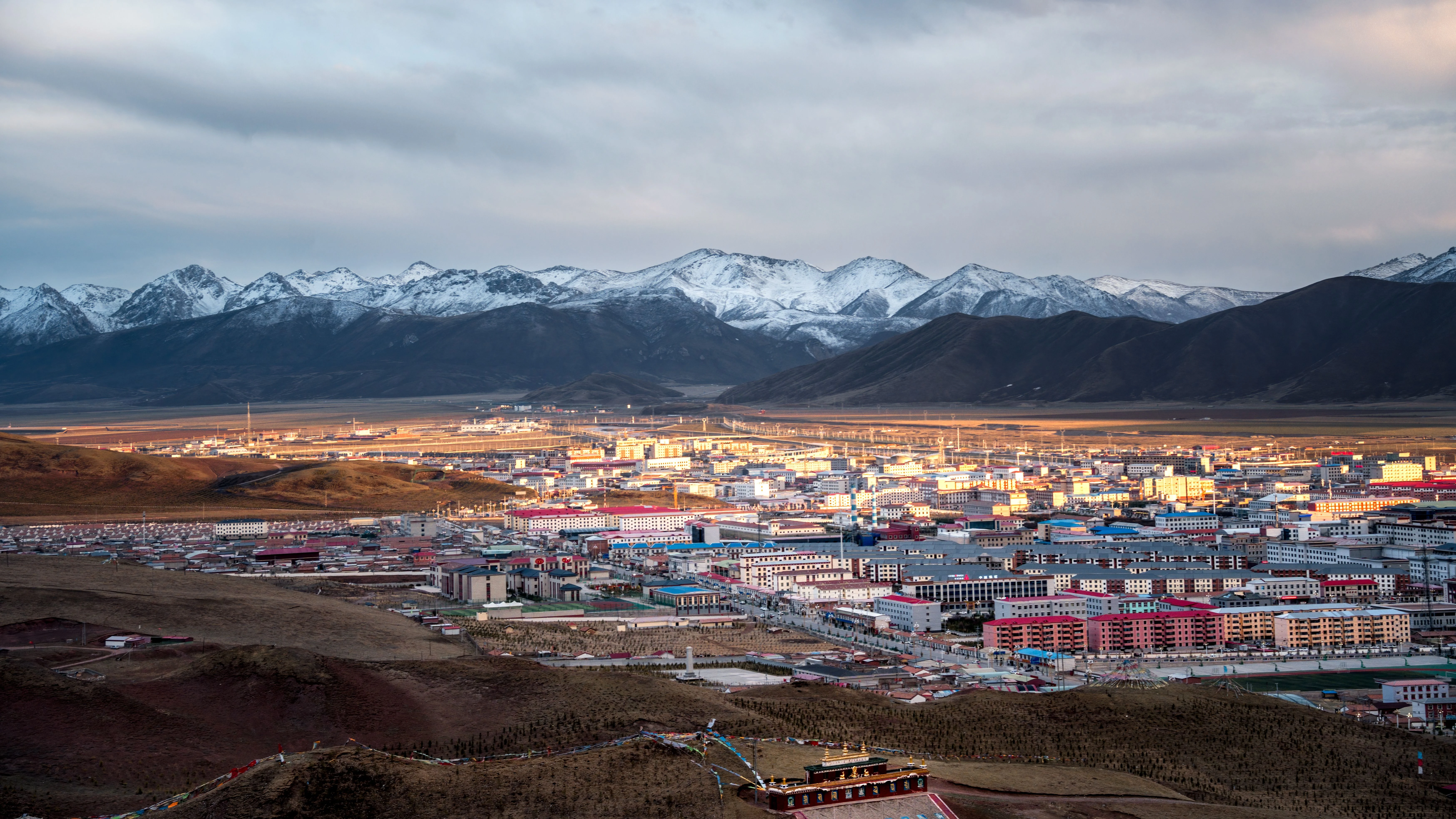 Une ville tib&eacute;taine sur le plateau du Qinghai entour&eacute;e de montagnes enneig&eacute;es au coucher du soleil, travers&eacute;e lors du Voyage vers le Toit du Monde
